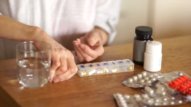 Retiree washes down a tablet with water from a glass. Pharmacy concept. Hands of an old woman on the background of bottles and blisters with pills - Filmagem, Vídeo