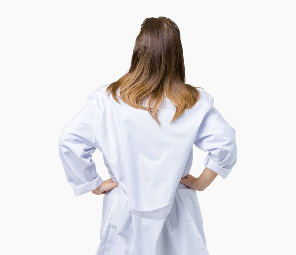 Középkorú érett doktor nő visel orvosi kabát, elszigetelt háttérben álló hátra keres el karral a test felett - Fotó, kép