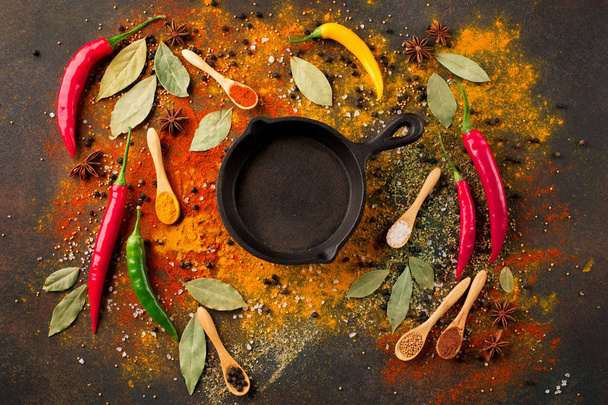 Herbs and spices selection (turmeric, paprika, Bay leaf, salt, chili pepper) and small black pan on dark rustic background, top view - Photo, Image