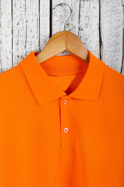 close up view of stylish orange shirt on hanger on wooden wall background - Photo, Image