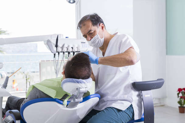 hammaslääkäri ja miespotilas toimenpiteen aikana hammashoitolassa
 - Valokuva, kuva