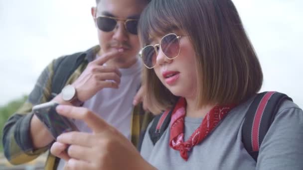 Ázsiai hátizsák pár vasútállomáson, fiatal édes pár turista hátizsákos mobiltelefon segítségével keresi és irányát térképeket útjukat Thaiföldön. Életmód pár pihenni és utazási koncepció. - Felvétel, videó