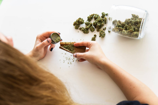 Woman rolling a marijuana blunt on white background. Close up of marijuana blunt with grinder. Cannabis use concept. Woman preparing and rolling marijuana cannabis joint. - Valokuva, kuva