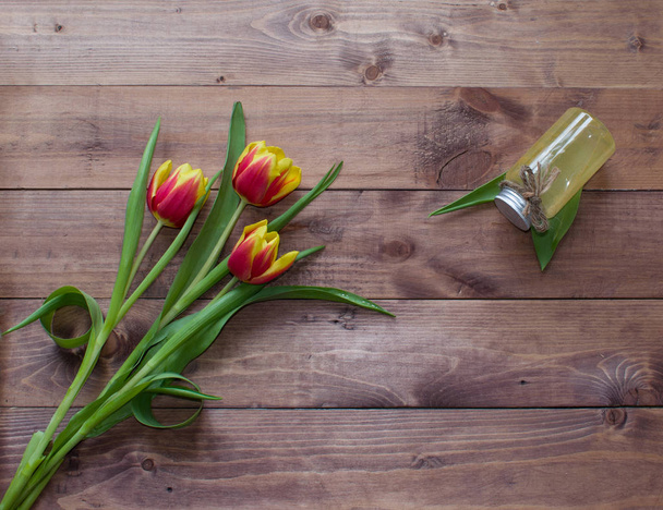 Ramo de primavera de flores de tulipán con producto cosmético sobre fondo de madera.Vista con espacio para copiar
 - Foto, Imagen