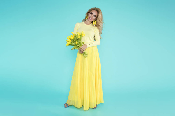 Spring Woman. Beauty Summer model girl with colorful clothes, holding a bouquet of spring flowers. Beautiful lady with yellow tulips on the blue background. - Foto, Imagem