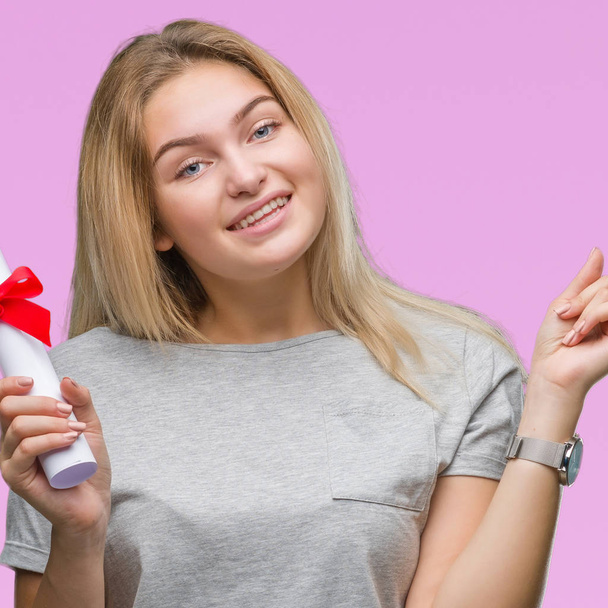 Young caucasian woman holding degree over isolated background very happy pointing with hand and finger to the side - Foto, Imagem