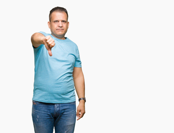 Hombre árabe de mediana edad vistiendo una camiseta azul sobre un fondo aislado que se ve infeliz y enojado mostrando rechazo y negativo con el gesto de los pulgares hacia abajo. Mala expresión
. - Foto, Imagen