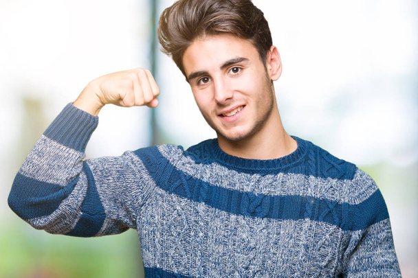 Young handsome man over isolated background Strong person showing arm muscle, confident and proud of power - Photo, Image