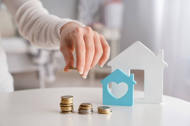Figure of house and woman stacking coins on table. Concept of buying property - Photo, Image