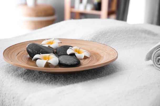 Prato com pedras de massagem e flores na mesa no salão de spa
 - Foto, Imagem