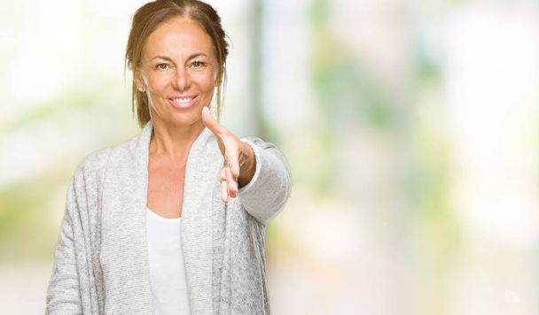 Взрослая женщина средних лет в зимнем свитере на обособленном фоне дружелюбно улыбается, предлагая рукопожатие в качестве приветствия и приветствия. Успешный бизнес
. - Фото, изображение