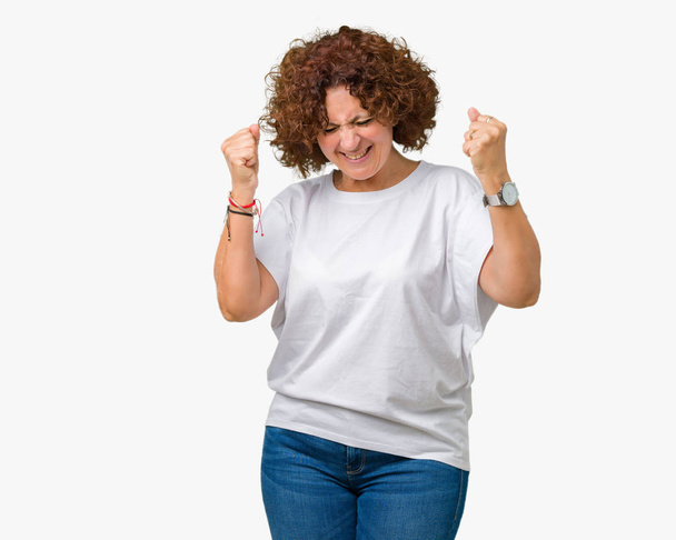 Bella donna anziana di mezza età che indossa t-shirt bianca su sfondo isolato molto felice ed eccitato facendo gesto vincitore con le braccia alzate, sorridente e urlando per il successo. Concetto di celebrazione
. - Foto, immagini