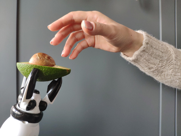 A robot's hand stretches an avocado into a young woman's hand, background or concept. - Fotoğraf, Görsel