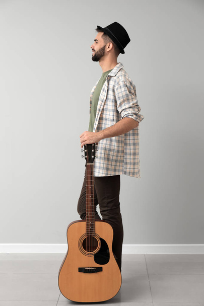 Handsome musician with guitar near light wall - Фото, зображення