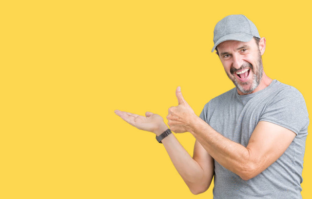 Handsome middle age hoary senior man wearing sport cap over isolated background Showing palm hand and doing ok gesture with thumbs up, smiling happy and cheerful - Photo, Image