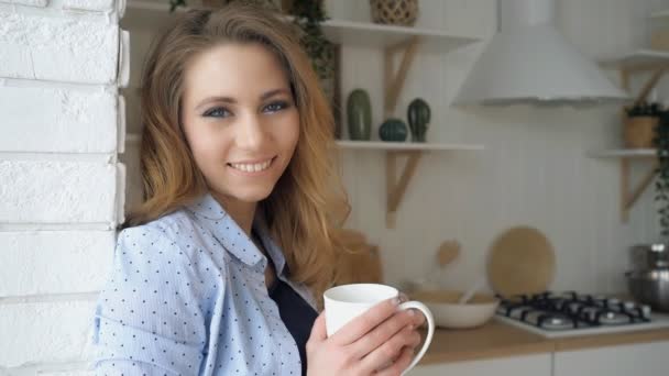 κορίτσι με χαλαρή τρίχα ποτά τσαγιού χαμόγελα ακουμπά στον τοίχο από τούβλα - Πλάνα, βίντεο