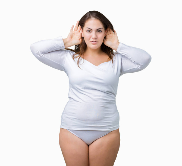schöne plus size junge übergewichtige Frau, die weiße Unterwäsche über isoliertem Hintergrund trägt und versucht, beide Hände am Ohr zu hören, neugierig auf Klatsch. Hörprobleme, Gehörlosigkeit - Foto, Bild