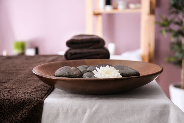 Prato com pedras de massagem e flor na mesa no salão de spa
 - Foto, Imagem