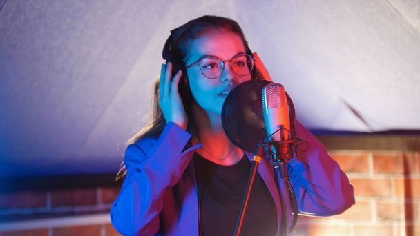 Молодая женщина в очках поет в неоновом свете в студии
 - Фото, изображение