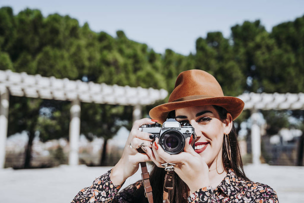 Χαμογελώντας νεαρή γυναίκα χρησιμοποιώντας μια φωτογραφική μηχανή για να τραβήξετε φωτογραφία. - Φωτογραφία, εικόνα