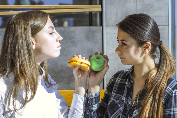dvě krásné dívky v kavárně jíst hamburger a apple, zdravé a nezdravé jídlo - Fotografie, Obrázek