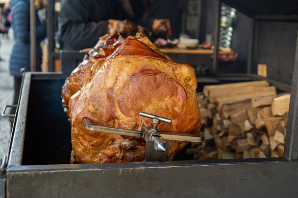 Large part of meat cooked on a rotate grill over open fire. Grilled   prepared outdoors. Smoked grilled Old Prague ham - Photo, Image