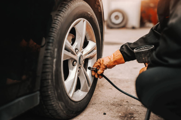 Close up of auto mechanic using tire pump on car tire in workshop. - Photo, Image