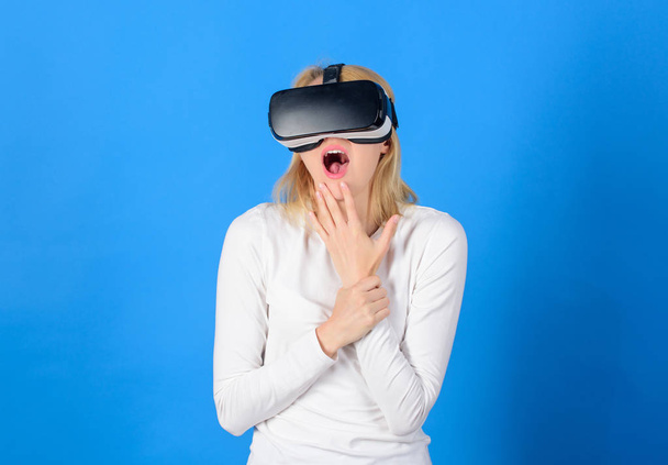 Vrouw dragen VR bril op blauwe achtergrond. Vrouw genieten van cyber leuke ervaring in vr. Verbaasd jonge vrouw raakt de lucht tijdens de Vr-ervaring. Technische netwerk. - Foto, afbeelding