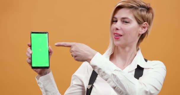 Woman pointing her finger to a smartphone with green screen on - Filmagem, Vídeo