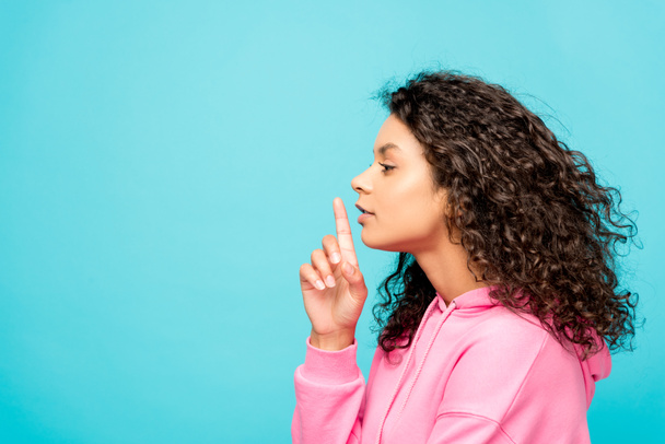 side view of curly african american girl showing hush sign isolated on blue  - Foto, afbeelding