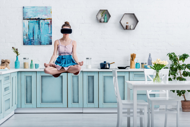 молодая женщина левитации в воздухе в позе лотоса и в гарнитуре виртуальной реальности
 - Фото, изображение