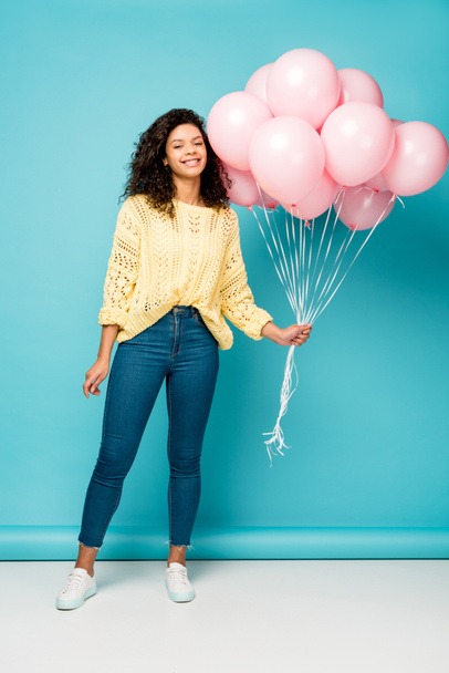 cheerful curly african american girl holding pink air balloons on blue - Foto, Bild