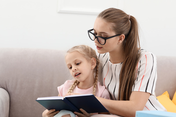 Маленька дівчинка з логопедом читає книгу в офісі
 - Фото, зображення