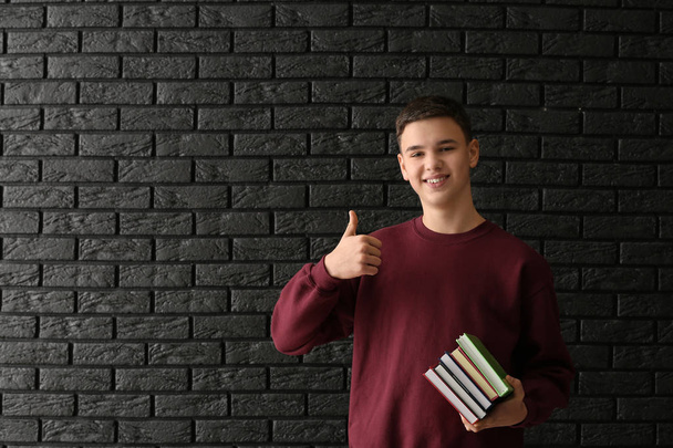 Estudante com livros mostrando polegar para cima no fundo escuro
 - Foto, Imagem
