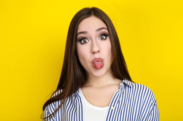 Beautiful young woman showing tongue on yellow background - Fotoğraf, Görsel