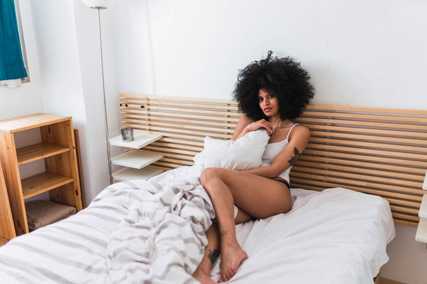 Young sensual black woman in lingerie lying on bed - 写真・画像
