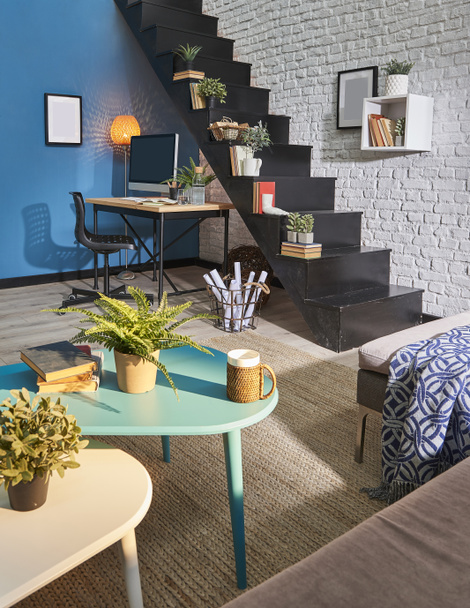 Sala de estar moderna, parede de tijolo branco, mesa de madeira e área de trabalho, escada preta, sofá tapete no interior
. - Foto, Imagem