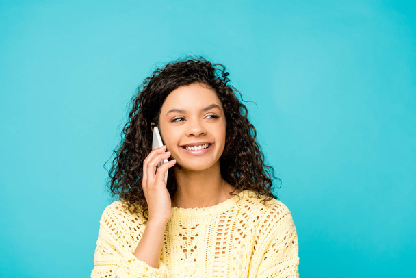 bastante rizado africano americano mujer sonriendo mientras habla en teléfono inteligente aislado en azul
  - Foto, imagen