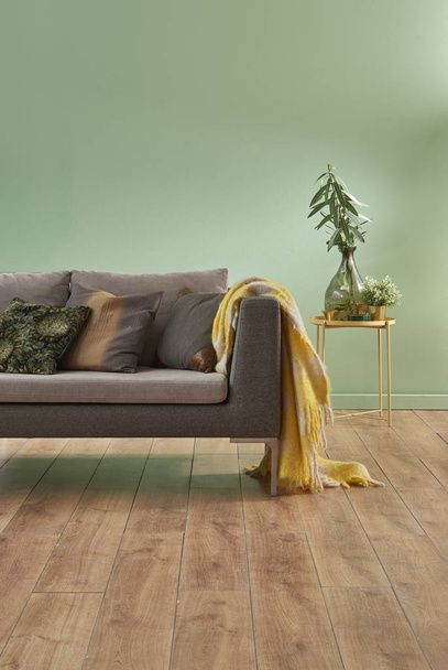 green wall and living room. Grey sofa with  blanket and vases of flowers. Study table and decorative white lamp. empty area for carpet - Photo, Image