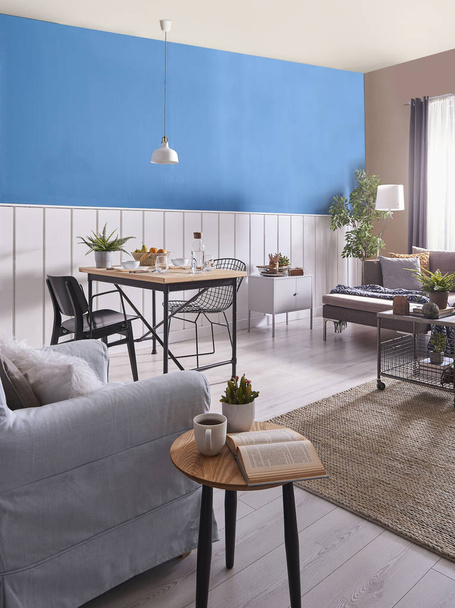 moderne Esszimmerdekoration, Holztisch und schwarzer Stuhl. blaue und weiße Wand Hintergrund. klassisches Wanddetail. graue Möbel, Mitteltisch, Sofa und blauer Sessel. Korbteppich und weiße Lampe. - Foto, Bild