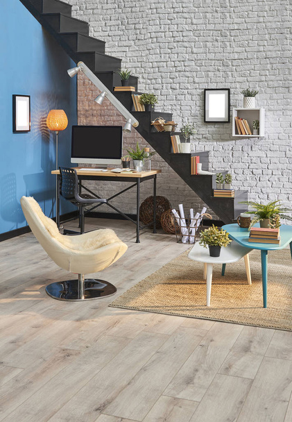 Sala de estar moderna, pared de ladrillo blanco, escritorio y escritorio de madera, escalera negra, sofá de alfombra en el interior
. - Foto, imagen