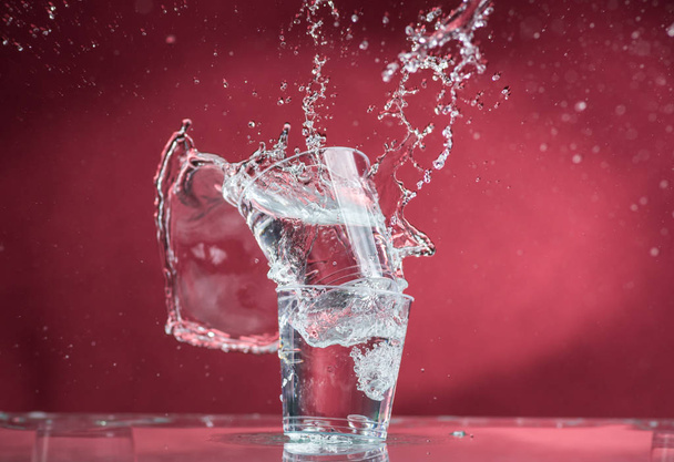 falling small glasses and spilling water on a red background - Fotoğraf, Görsel