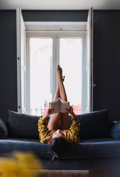 Young woman with book lying on sofa - Foto, Imagem