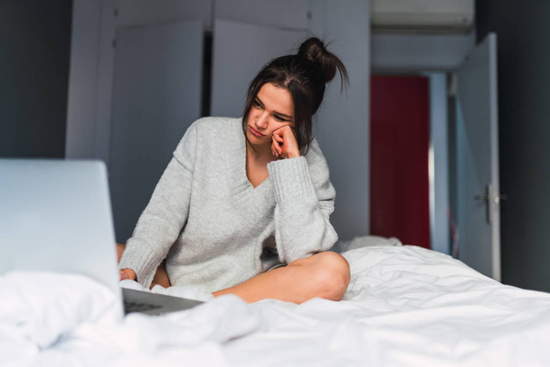 Young sad woman using laptop on bed - Fotó, kép