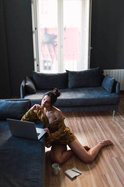 Young slim woman using laptop near sofa and cup on floor - Фото, зображення