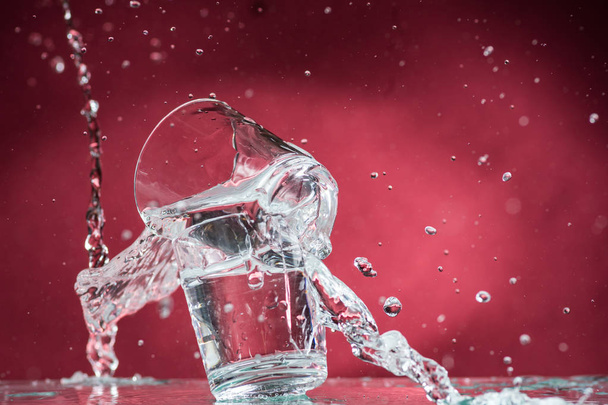 vallende kleine glazen en morsen water op een rode achtergrond - Foto, afbeelding