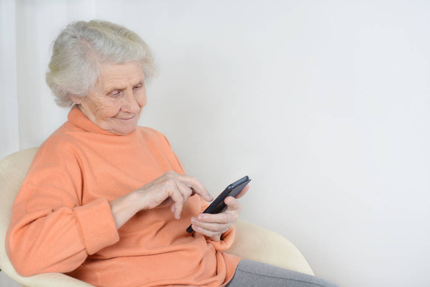 Senior woman is sitting and reading the latest news on her phone - Фото, изображение