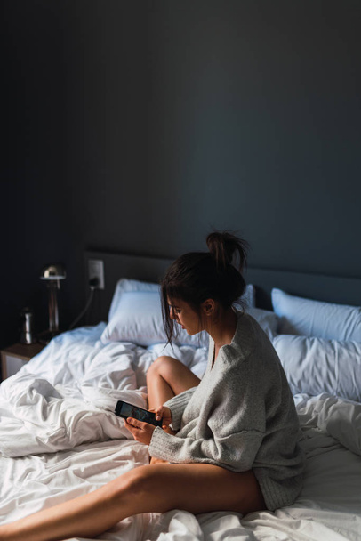 Young woman with smartphone sitting on bed - Foto, Bild