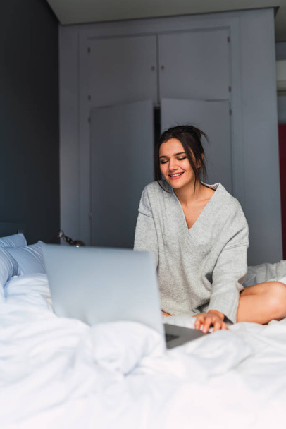 Young smiling woman using laptop on bed - Photo, Image