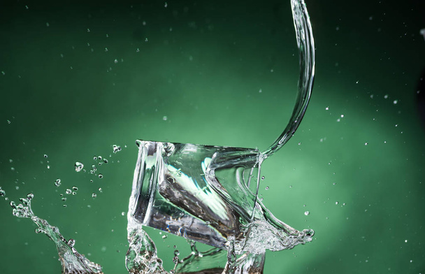 cayendo pequeño vidrio transparente con agua clara y derramando agua sobre un fondo verde
 - Foto, imagen